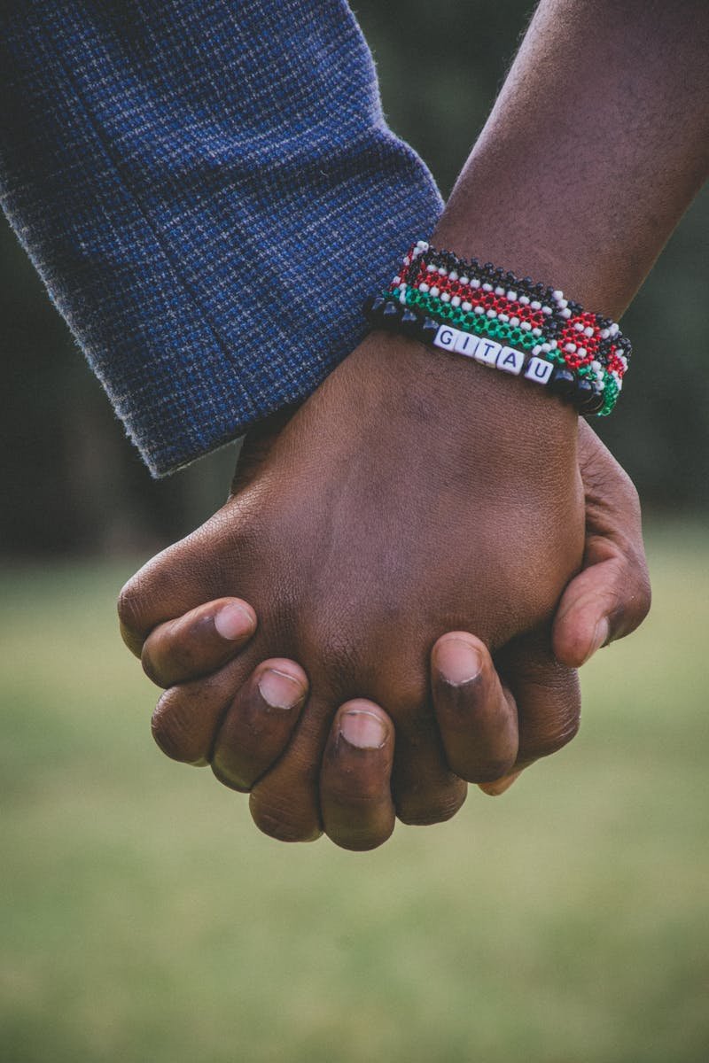 Close-up view of a couple holding hands with beaded bracelets, symbolizing unity and love.